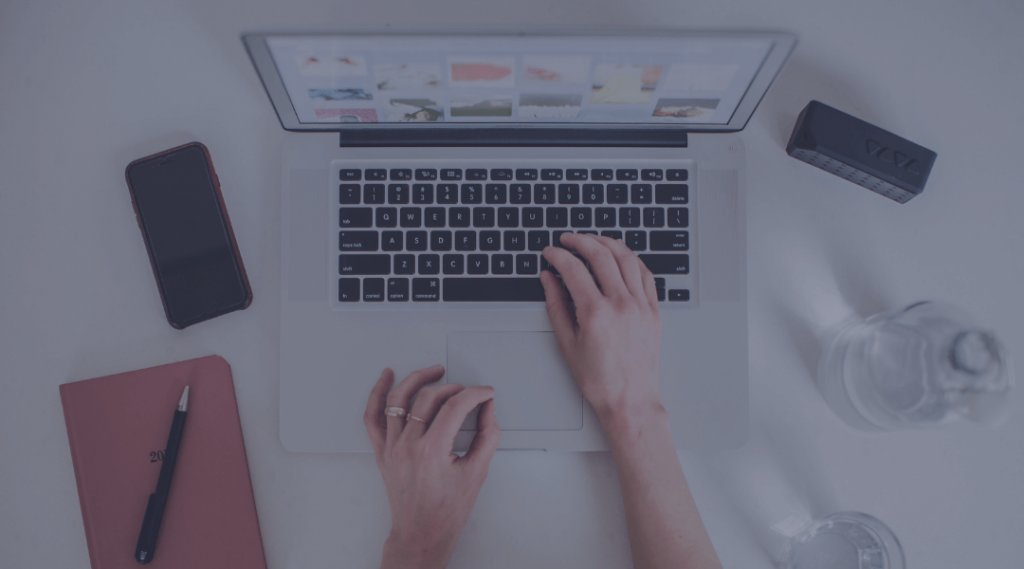 Hands typing on laptop, next to phone and agenda